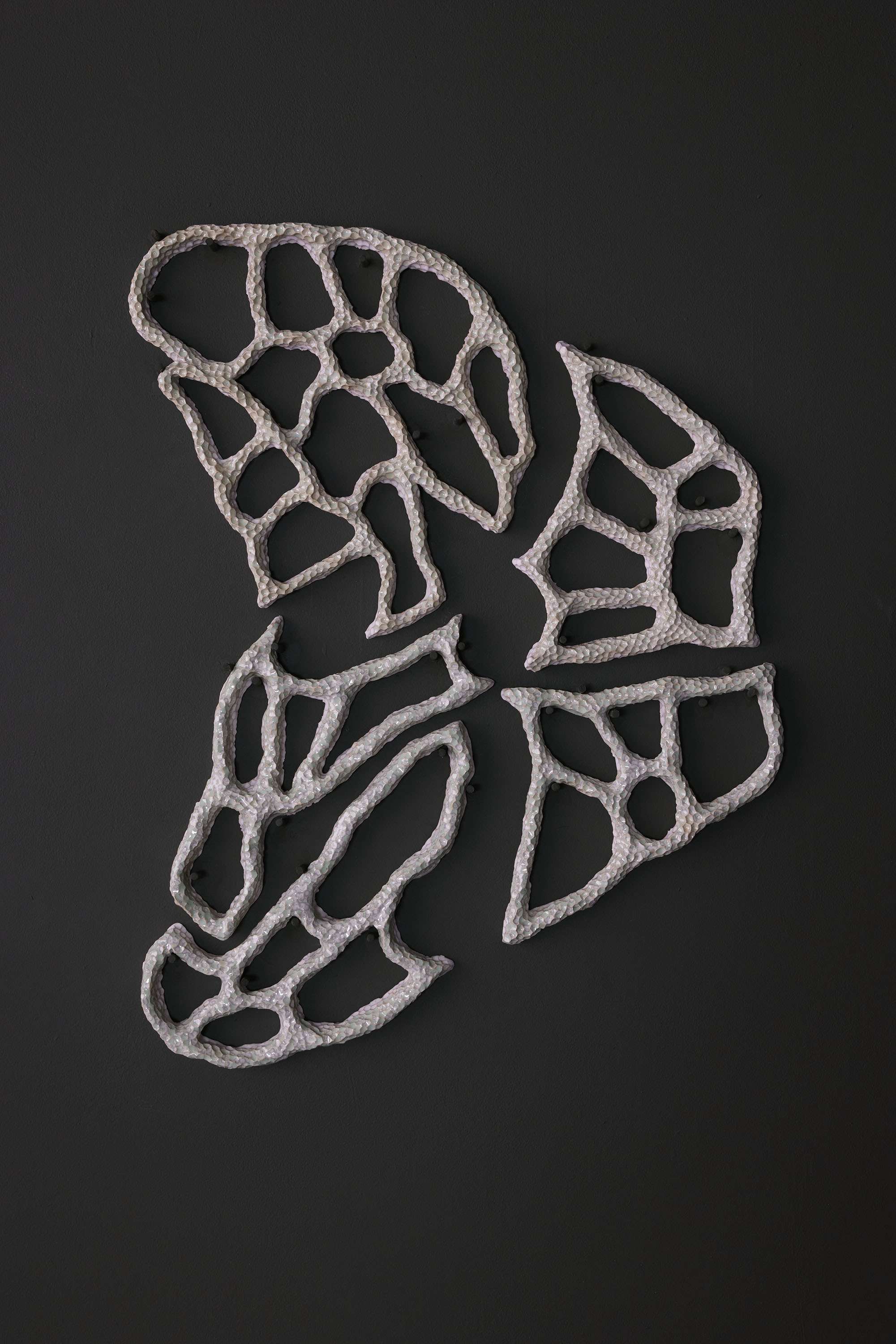 Image shows a ceramic shape mounted on a dark green wall with a dimpled surface.