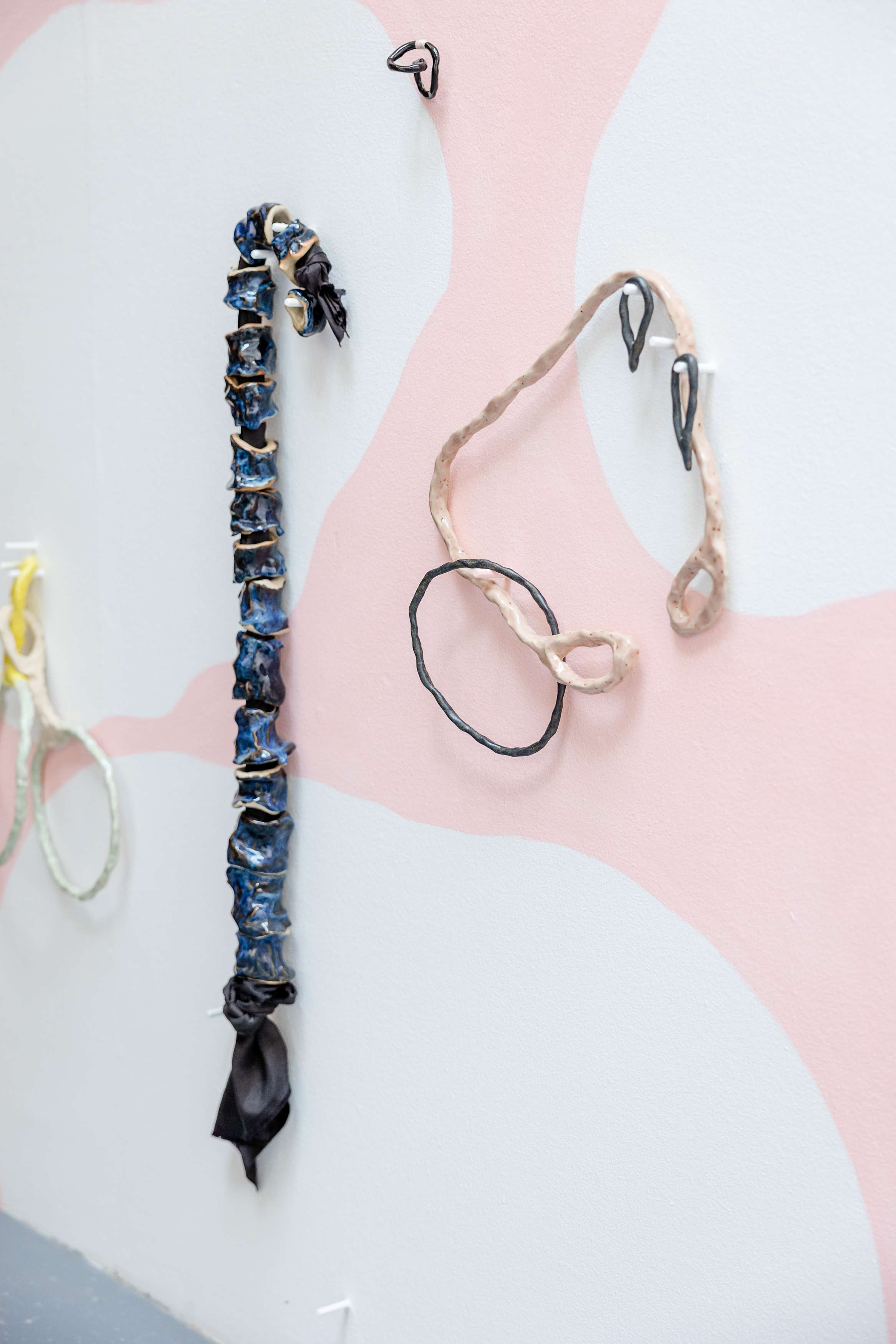 Image shows detail of a wall with white clouds retreating over a pink sky hung with drawn sculptural shapes. The objects include a spine, tears, hoops and a pelvis.